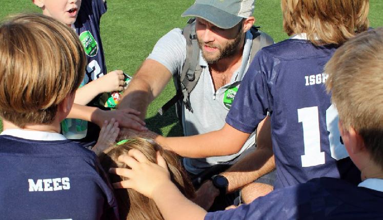 Zach and his young soccer protegees stack hands in a huddle on the field.