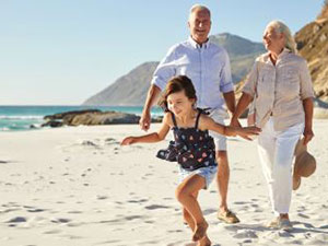 Happy couple enjoying a walk on the beach with their young granddaughter.